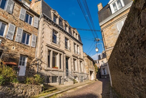 Une ruelle pavée bordée d’immeubles anciens en pierre, dotés de nombreuses fenêtres et de volets.