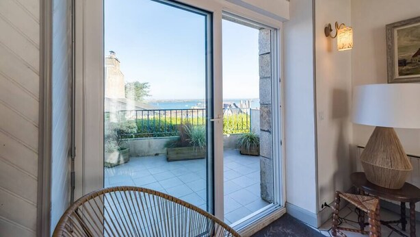 Ein Balkon mit Meerblick, ein Korbstuhl und ein Tisch mit einer Lampe.