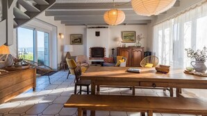 Ein großzügiger Wohnbereich mit Esstisch aus Holz, gemütlicher Sitzgelegenheit, Kamin und großen Fenstern mit Aussicht.