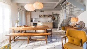 Eine moderne Küche mit Holzausstattung und einer zentralen Kochinsel, ein Essbereich mit Holztisch und Bänken sowie eine Treppe, die zu einer oberen Ebene führt.