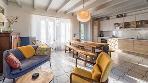 Ein modernes Wohnzimmer mit einer Couch, einem Holztisch und einem Sessel. Es gibt eine Küchenzeile mit Schränken und einem Fenster.