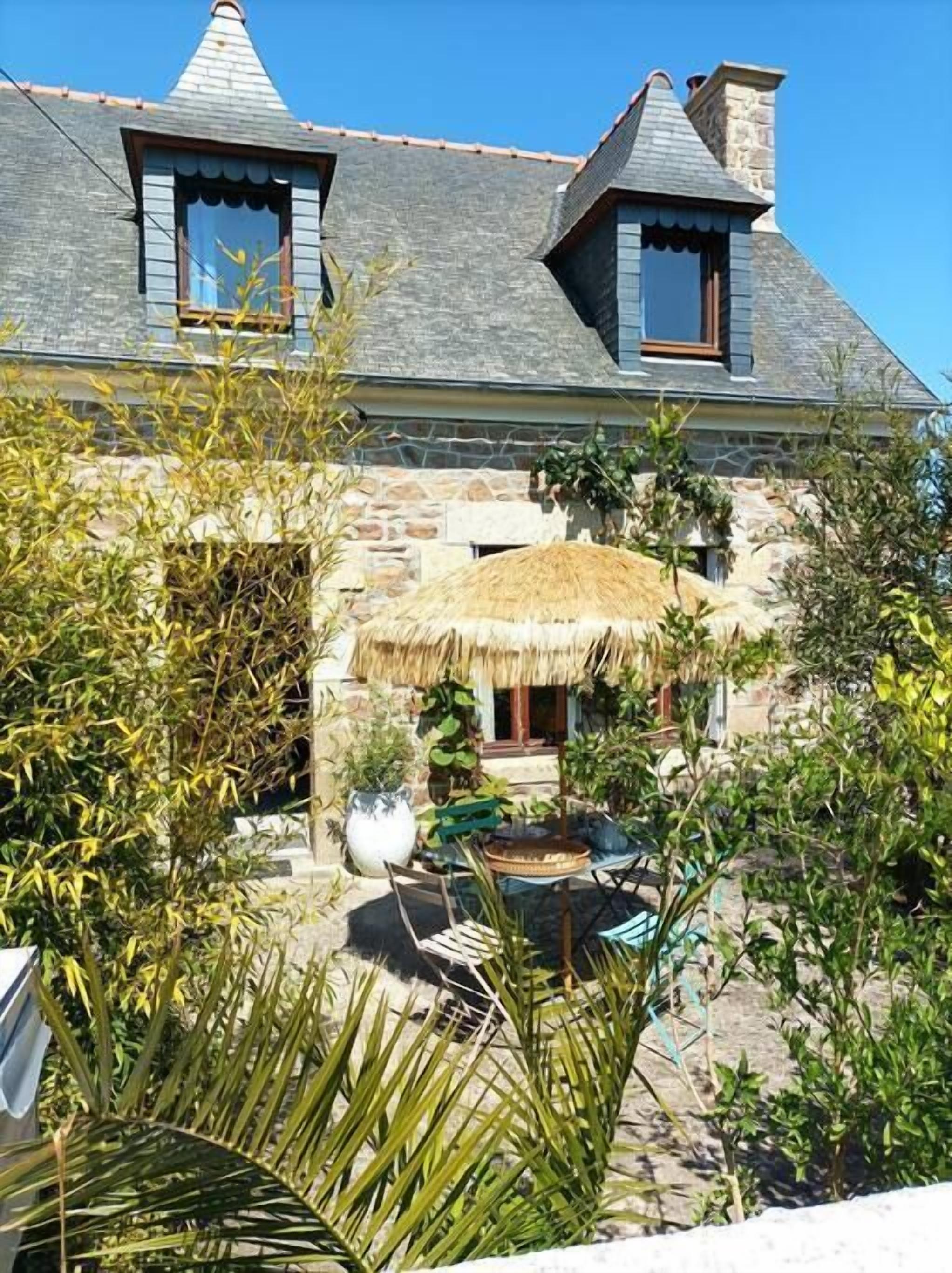 Ein Haus aus Stein mit einem Reetdach, einer Steinterrasse und einem kleinen Garten mit Pflanzen und einem Tisch.