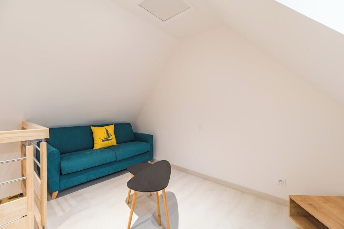 Une petite pièce lumineuse, avec un canapé bleu, une chaise noire et une étagère en bois.