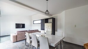 A modern living room with a sofa, a dining table with chairs, and a kitchen area with cabinets. - Vacation home in Pordic - close to the sea (Pordic)