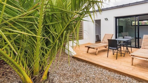 A modern outdoor patio with a wooden deck, a table with chairs, and a palm tree. - Vacation home in Pordic - close to the sea (Pordic)