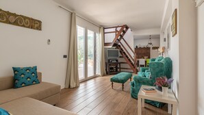 A living room with a wooden staircase, a sofa, a green armchair, and a small table with a book and flowers. - Villa Giovanna con Piscina by Wonderful Italy (Castellammare del Golfo)