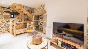 Una sala de estar acogedora con una pared de piedra, una escalera de madera, un televisor y un área de descanso confortable.