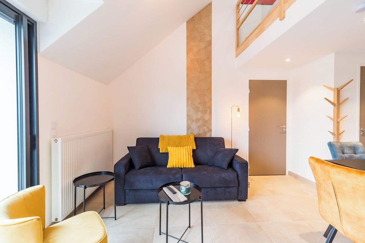 A modern living room with a dark sofa, a yellow throw, a small round table, and a yellow chair.
