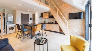 Eine moderne Wohnung mit Küche, Essbereich und Wohnzimmer. Sie verfügt über eine Treppe, eine Waschmaschine und einen Flachbildfernseher.