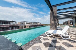 A swimming pool with a checkered floor, lounge chairs, and a view of buildings in the background. - Casa Lucho, Live The Good Life! (Tulum)