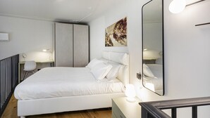 A modern bedroom with a large bed, bedside tables with lamps, a wall-mounted mirror, and a painting. - Loft Garibaldi by Wonderful Italy (Genova)