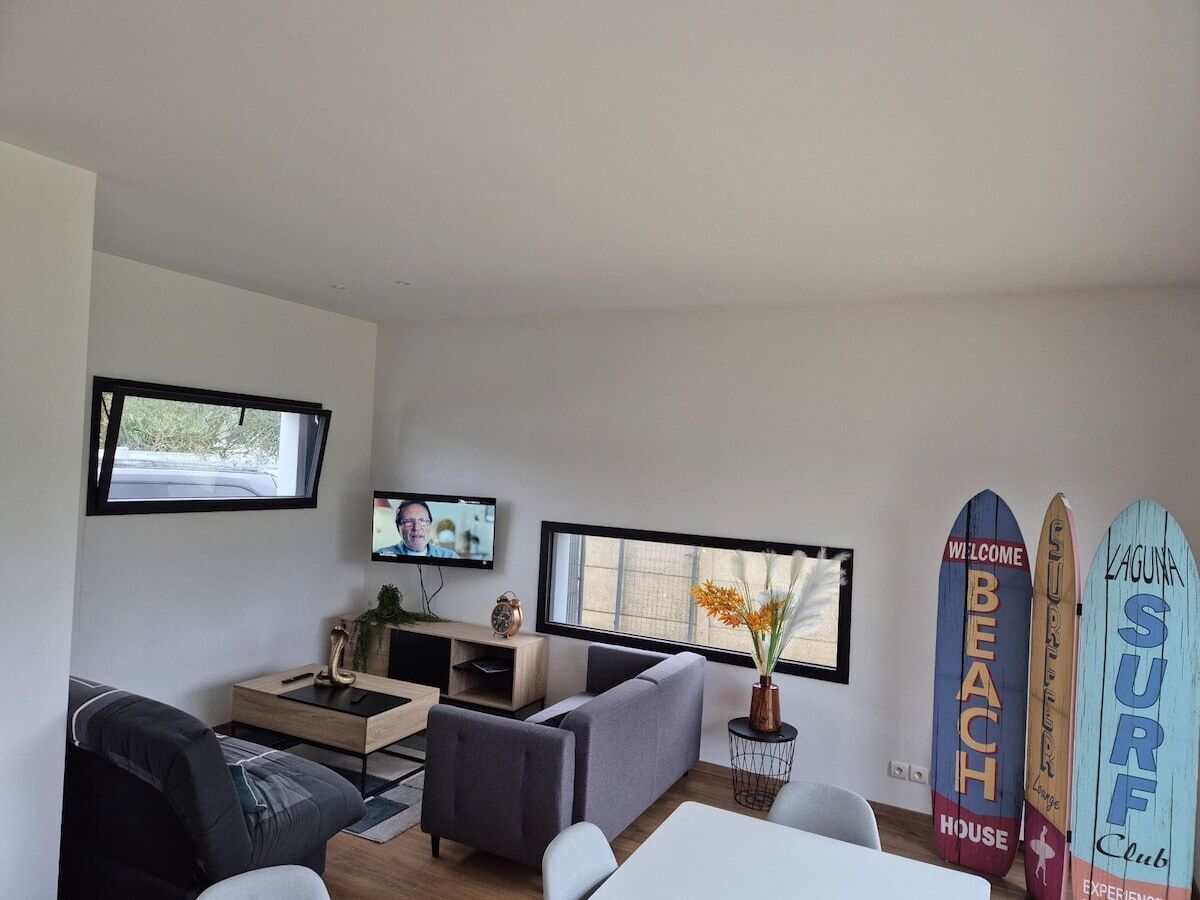 Een moderne woonkamer met een bank, salontafel en televisie. Op de muur staan surfplanken en een raam zorgt voor natuurlijk licht.