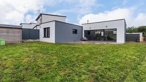 Ein modernes, zweistöckiges Haus mit Flachdach, großen Fenstern und einer überdachten Terrasse.