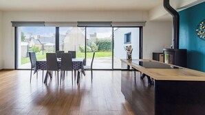 Eine moderne Küche mit einem schwarzen Herd, einem Holzespeisesaal mit Stühlen und Blick durch große Glasüren nach draußen.