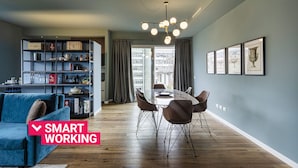 A modern living room with a dining area, featuring a blue sofa, a glass table, and a bookshelf with various items. - Carignano Luxury Suite by Wonderful Italy (Genova)