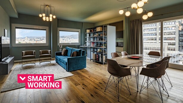 A modern living space with a dining area, a blue sofa, a bookshelf, and large windows offering city views. - Carignano Luxury Suite by Wonderful Italy (Genova)