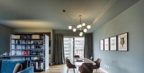 Una sala de estar moderna con comedor, que incluye un sofá azul, una mesa de vidrio y una estantería con varios objetos.