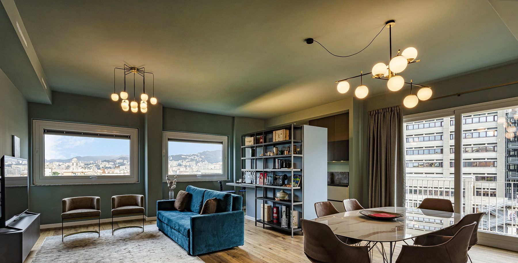 Un espace de vie moderne comprenant un coin repas, un canapé bleu, une bibliothèque et de grandes fenêtres offrant une vue sur la ville.