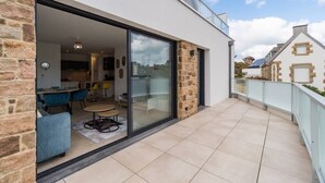 Une maison moderne avec une porte vitrée donnant sur un coin repas agrémenté de chaises bleues et d’une table ronde.