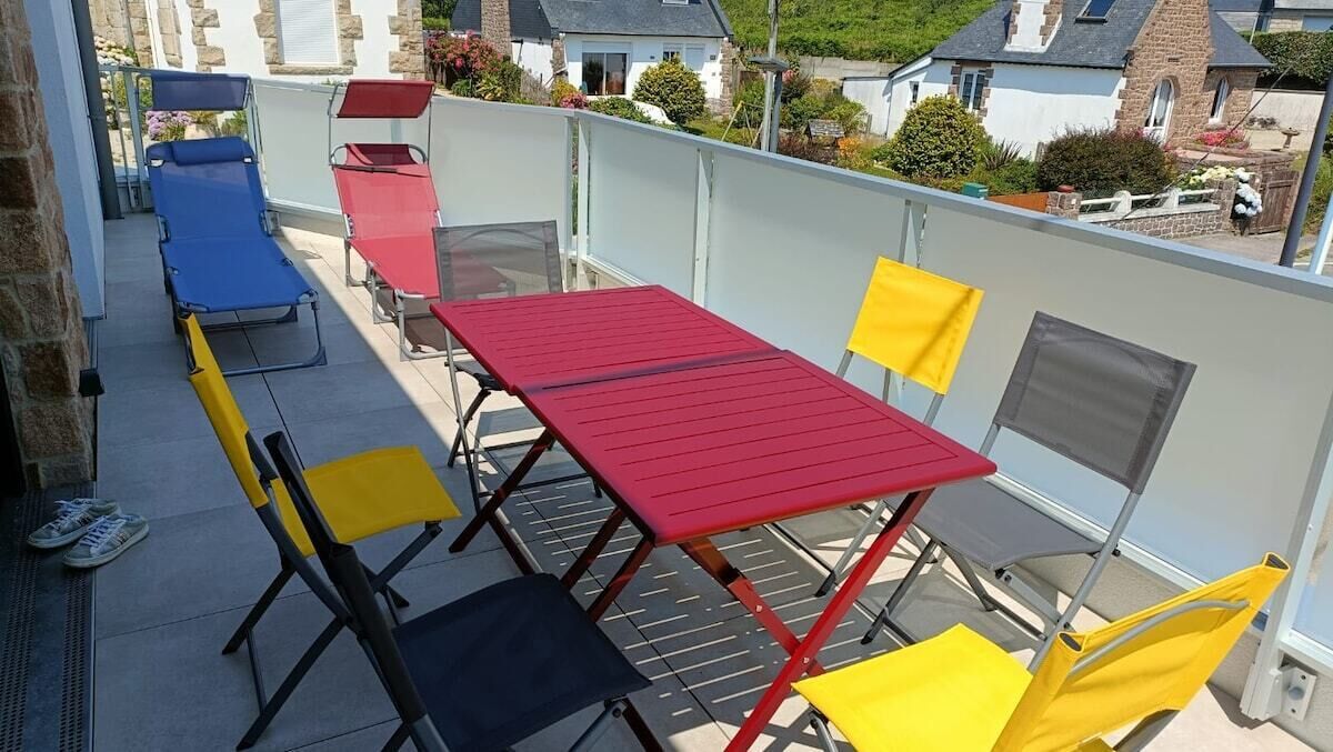 A balcony with a red table and yellow chairs, a blue lounge chair, and a red folding chair.