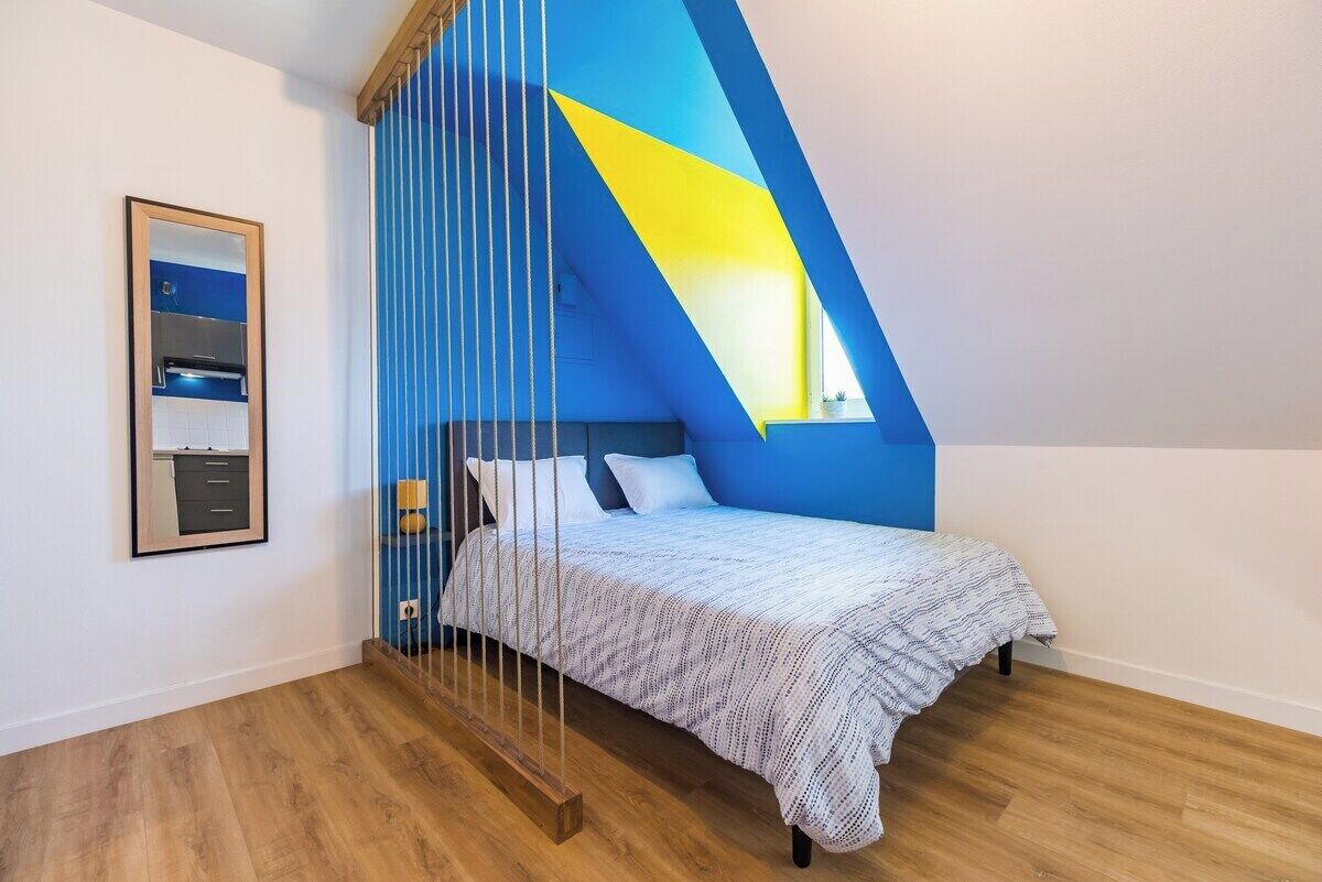 A bedroom with a sloped ceiling, a bed with a white patterned bedspread, a nightstand, and a mirror on the wall.
