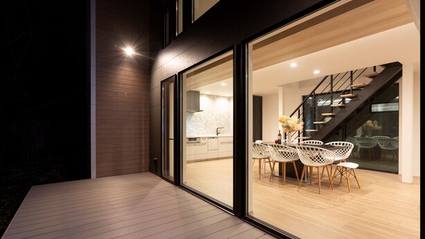 A modern house with a large glass door leading to a dining area with white chairs and a table. - Hakone Ashinoko Lakeside Resort (Hakone)