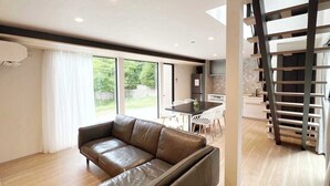 A modern living room with a leather sofa, a dining table with chairs, and a kitchen area visible through an open door. - Hakone Ashinoko Lakeside Resort (Hakone)