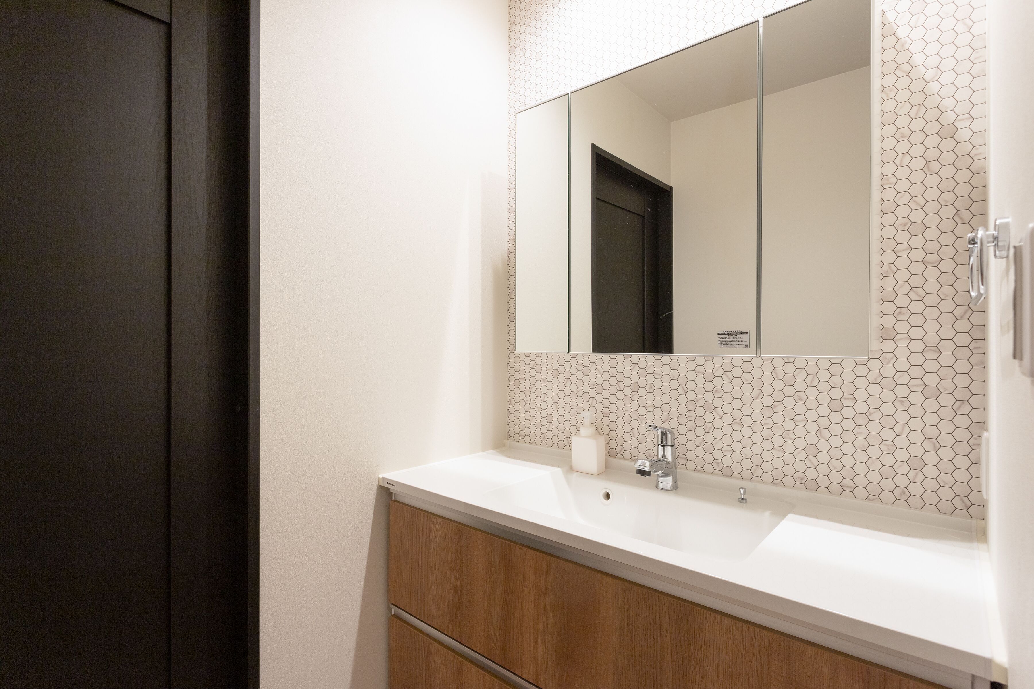 A bathroom with a white sink, a mirror, and a hexagonal tile backsplash.