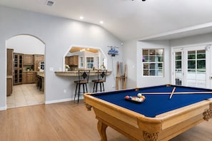 A pool table in a room with a kitchen and a dining area.