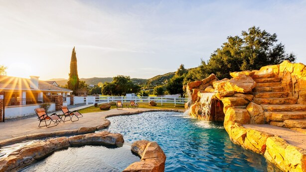 Una piscina con cascata artificiale, circondata da rocce e un recinto bianco.
