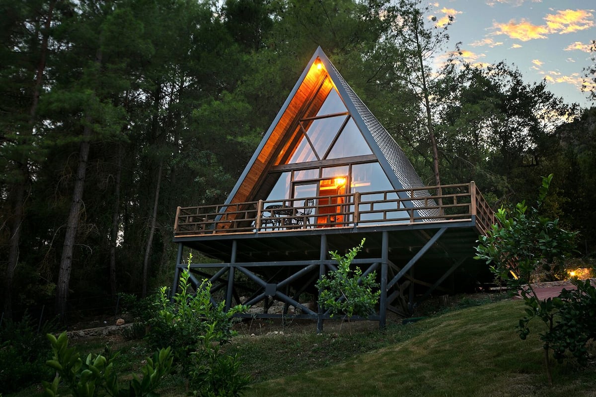 A modern, triangular glass house with a wooden deck and a visible interior.