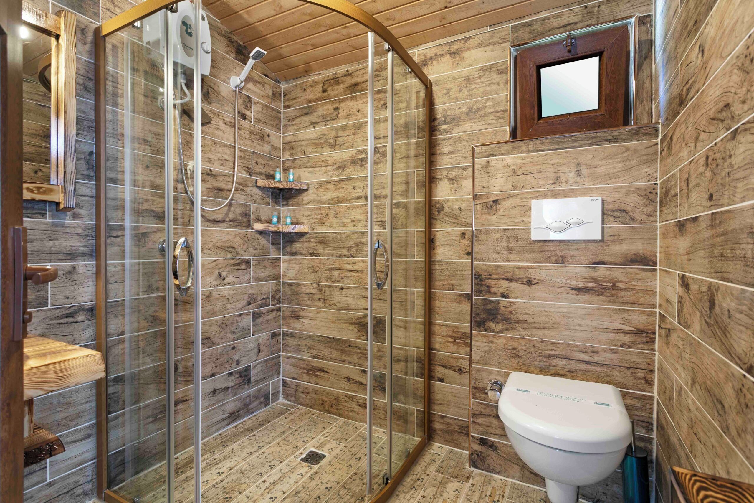 Un baño con ducha de vidrio, azulejos de madera, un inodoro y un estante pequeño con artículos de aseo.