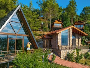 A modern house with a triangular glass facade, wooden balconies, and stone walls. - Botanik Gol Evleri (Bucak)