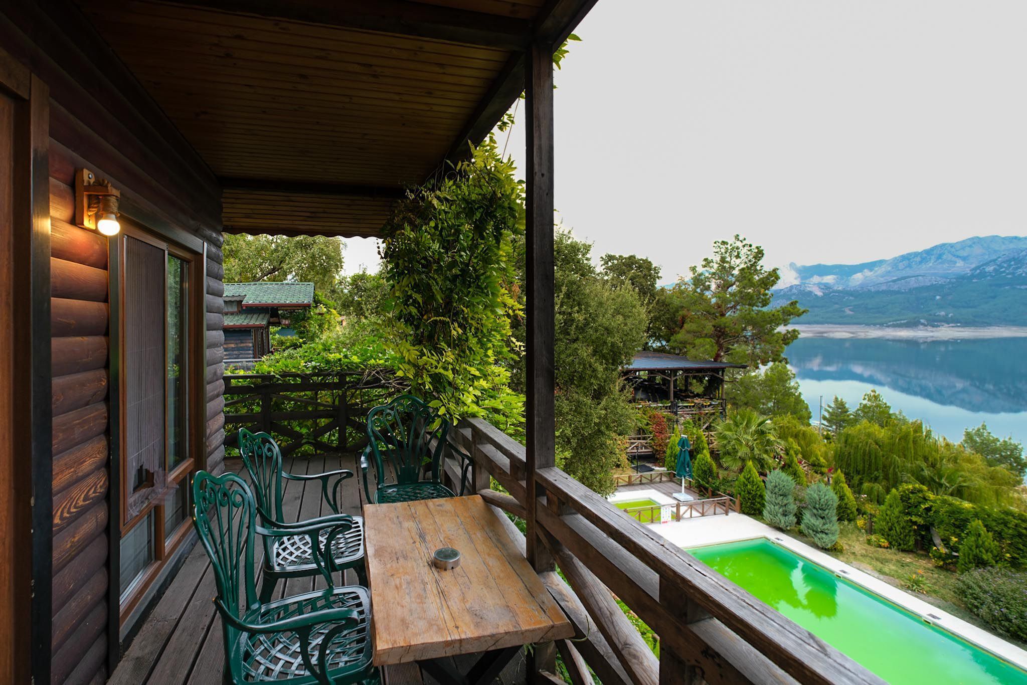 Una terraza de madera con una mesa y sillas, con vista a una piscina y un paisaje montañoso.