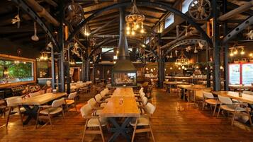 Un interior rústico con mesas y sillas de madera, una mesa central grande y un lámpara colgante.