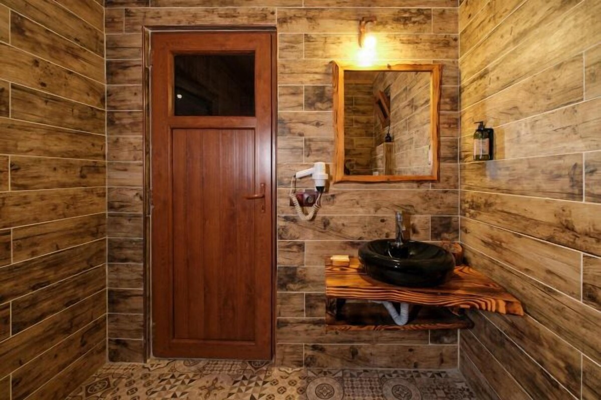 A bathroom with wooden walls, a wooden door, a sink with a basin, a mirror, and a towel rack.