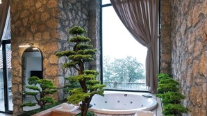 A spa area with a stone wall, wooden benches, a hot tub, and a view through a window. - Botanik Gol Evleri (Bucak)
