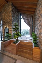 Un área de spa con pared de piedra, bancos de madera, una bañera de hidromasaje y vistas a través de una ventana.