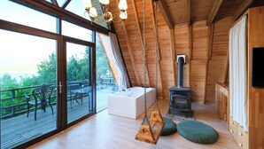 A spacious loft bedroom with a large window, a hanging swing chair, a wood-burning stove, and a white bathtub. - Botanik Gol Evleri (Bucak)