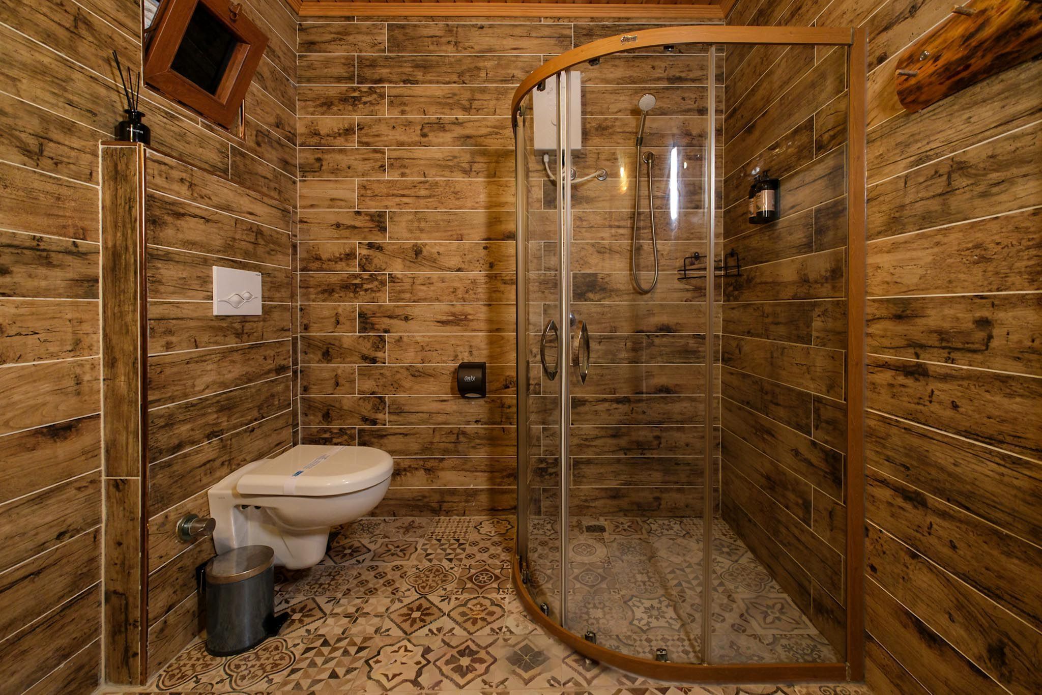 Een betegelde badkamer met houten lambrisering, een toilet, een douchecabine en vloertegels met een patroon.