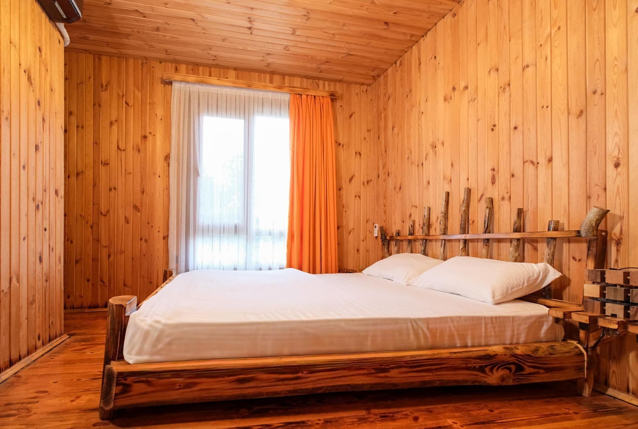 A wooden room with a bed, curtains, and a window.