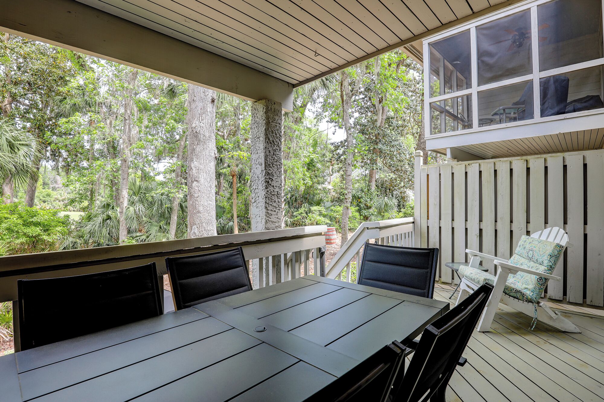 A covered outdoor dining area with a table and chairs, overlooking a forested area.