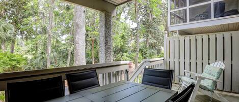 A covered outdoor dining area with a table and chairs, overlooking a forested area.