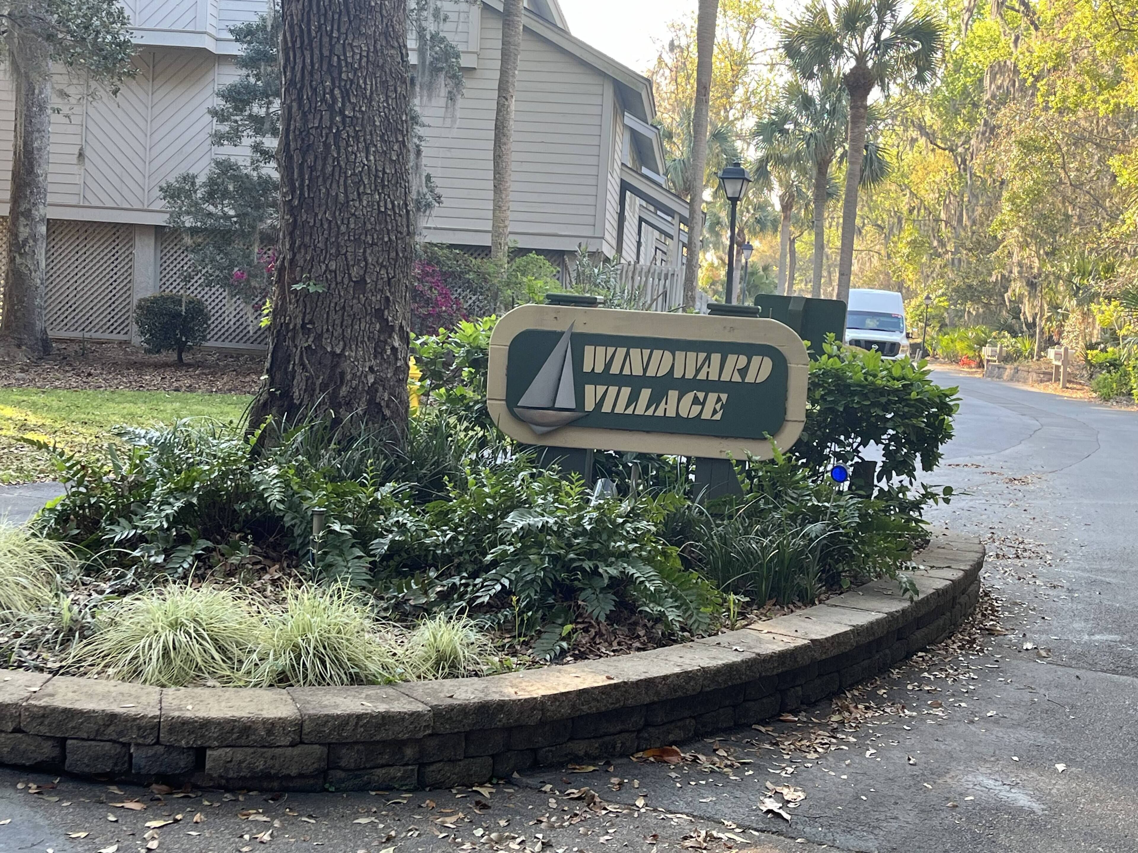 Señal de Windward Village con un área ajardinada que presenta un árbol y arbustos.
