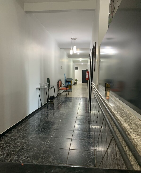 A hallway with a marble floor, a fire extinguisher, a chair, and a cart with cleaning supplies.