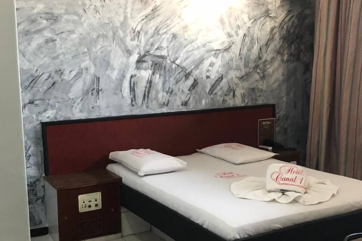 A hotel room with a large bed, a nightstand, and a wall with a textured mural.