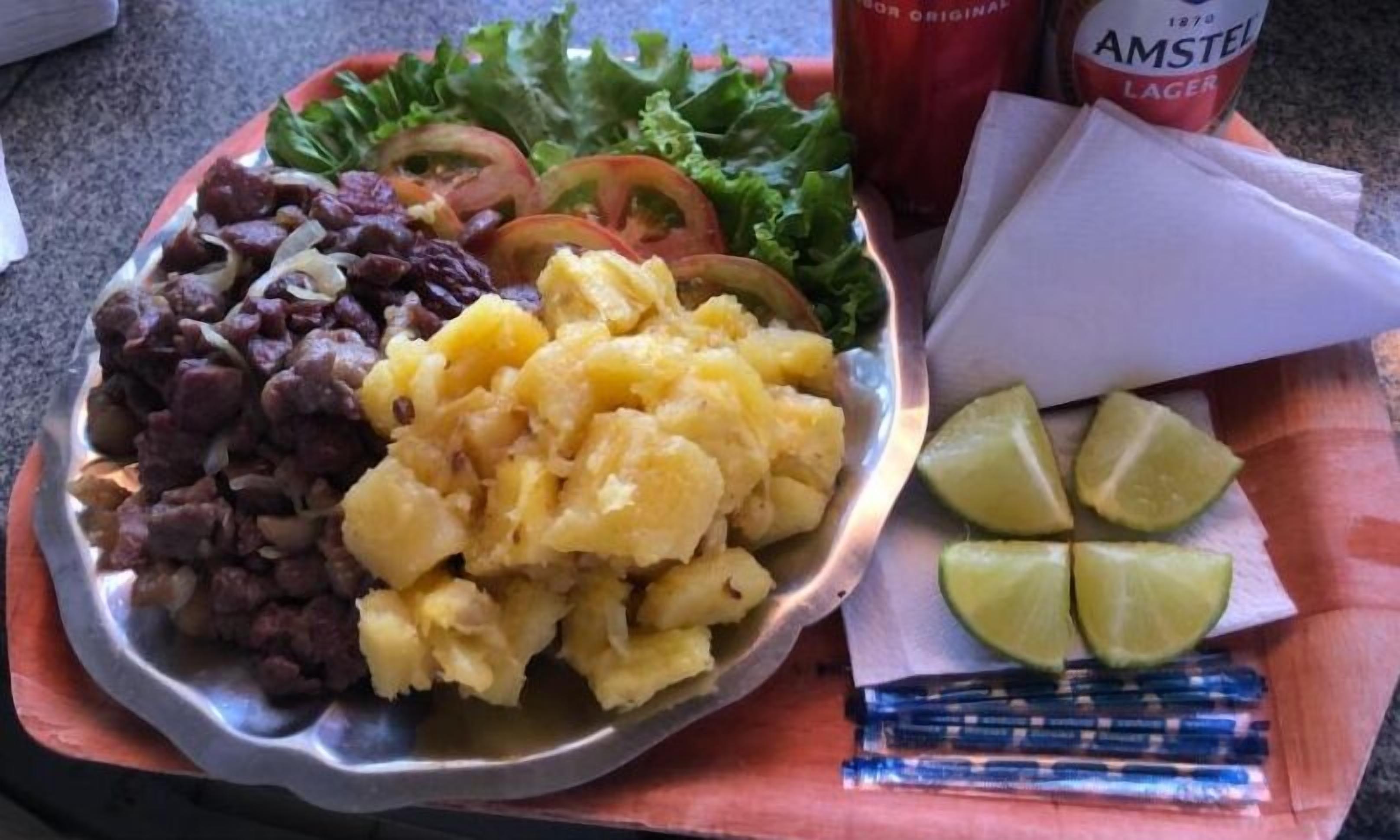 Un repas composé de haricots, de purée de pommes de terre et d’une salade à la tomate et à la laitue, servi dans une assiette en métal.