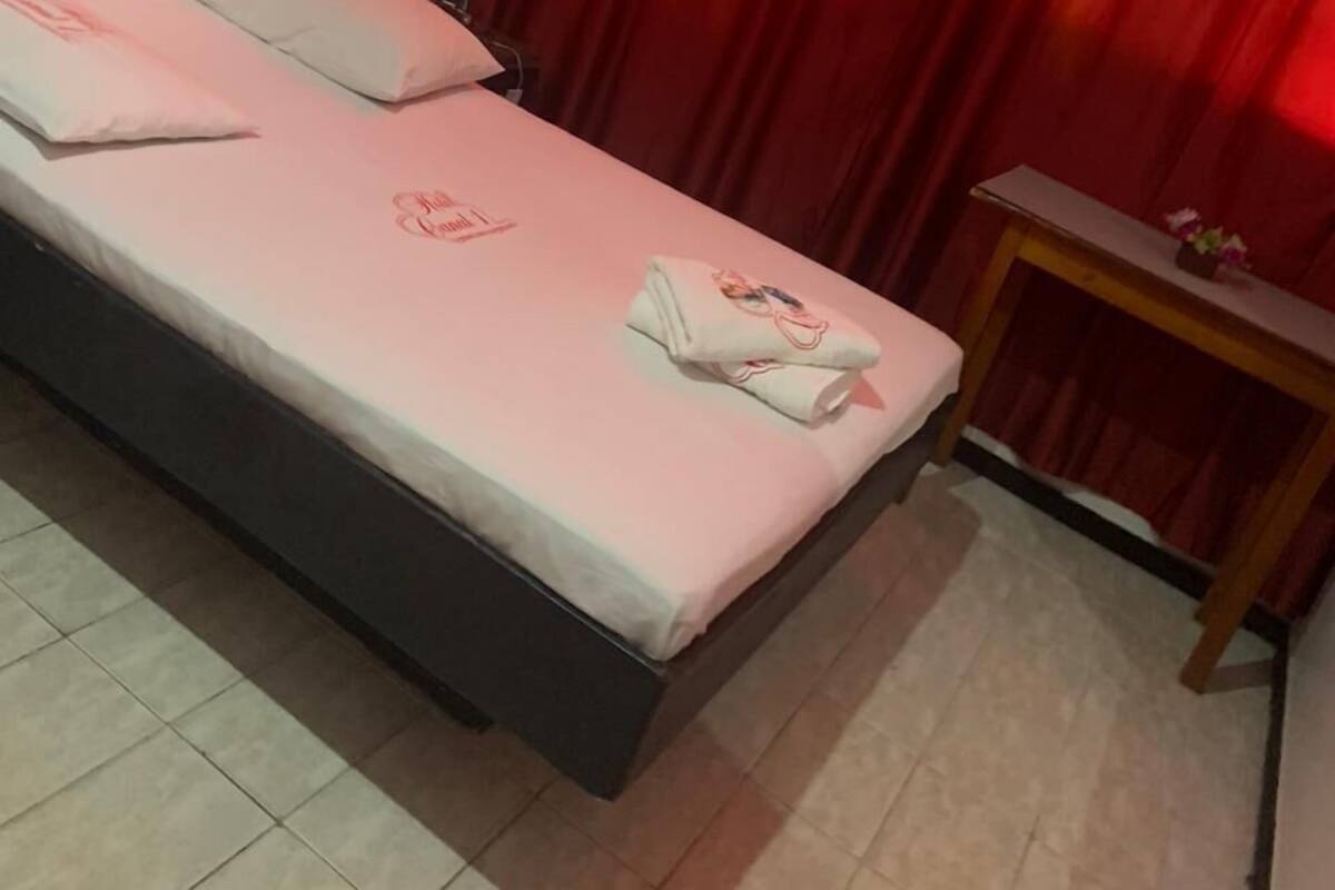 A bedroom with a bed, pillows, a bedside table, and a red curtain.