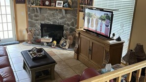 A living room with a stone fireplace, a television, a wooden coffee table, and a red sofa. - The  “MERMAIDS LAIR” (Rehoboth Beach)