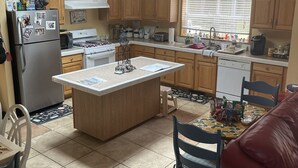 A kitchen with wooden cabinets, a refrigerator, a stove, and a dining area with a table and chairs. - The  “MERMAIDS LAIR” (Rehoboth Beach)